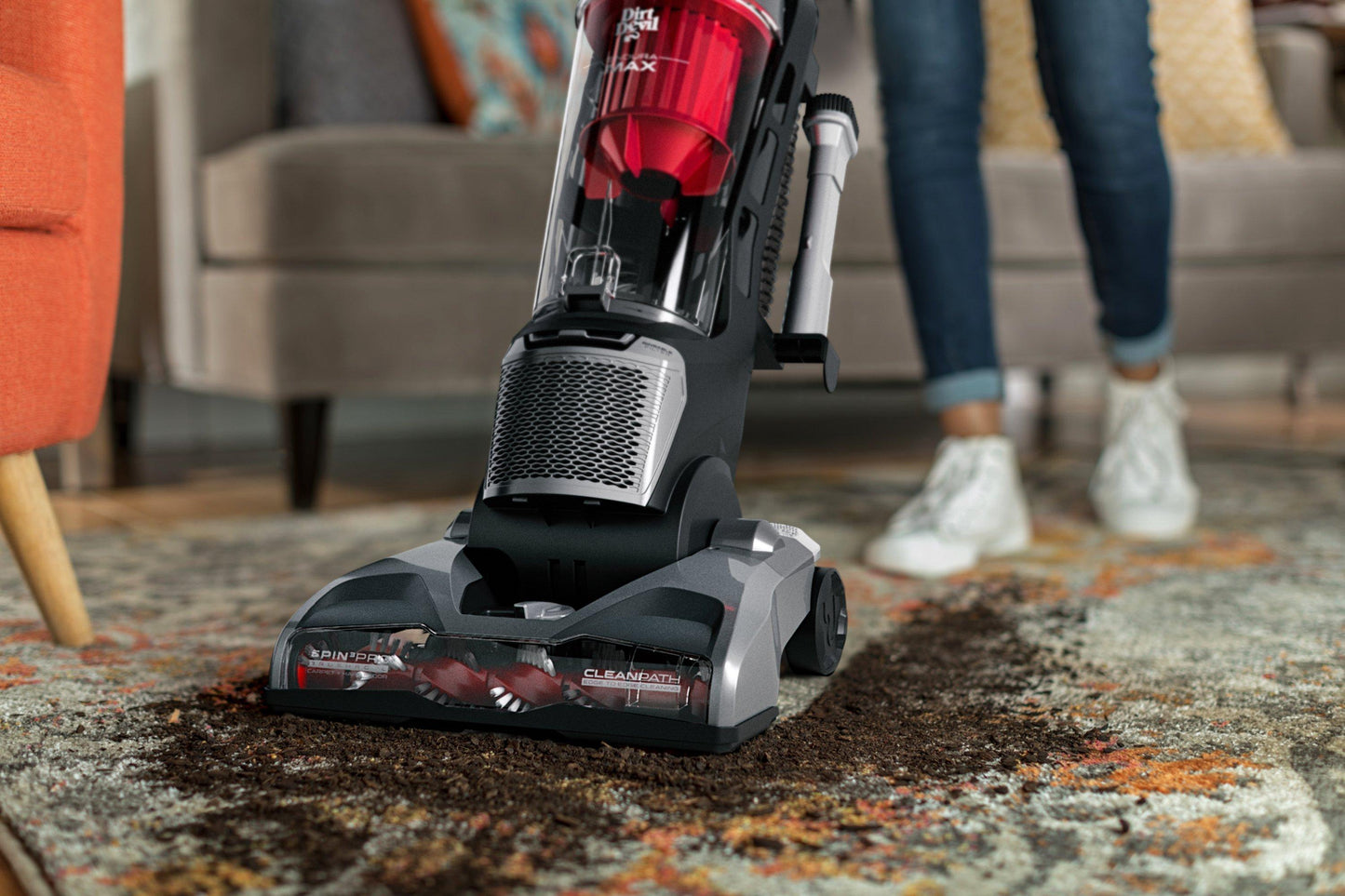 A red, silver and black upright vacuum cleans up spilled soil on a carpet
